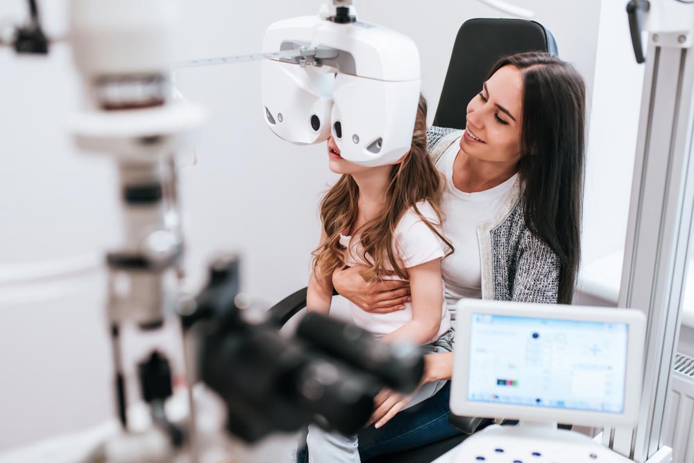 young woman and little cute girl are checking the eye vision in modern clinic