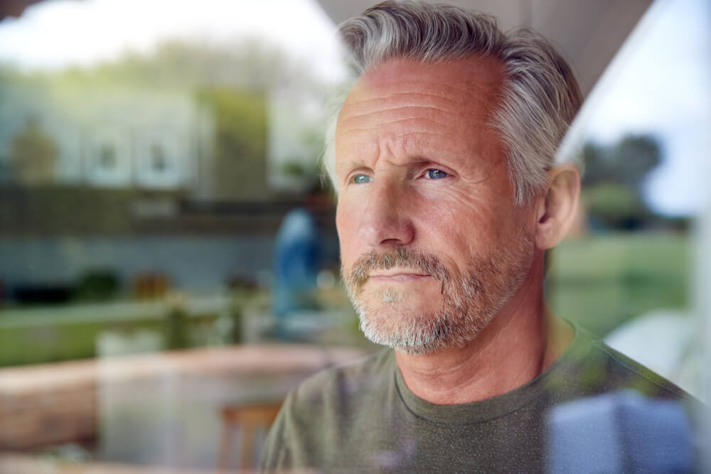 Senior Man Standing And Looking Out Door Viewed