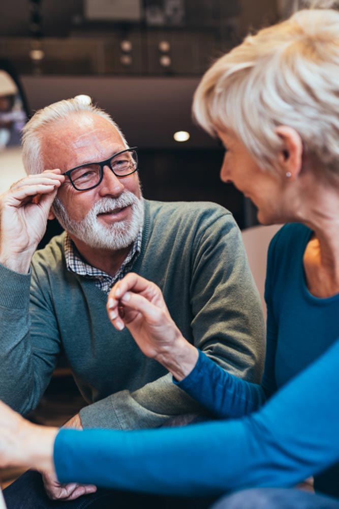 Happy senior couple choosing together eyeglasses frame in optical store