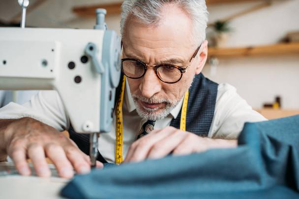 serious handsome tailor sewing cloth with sewing machine