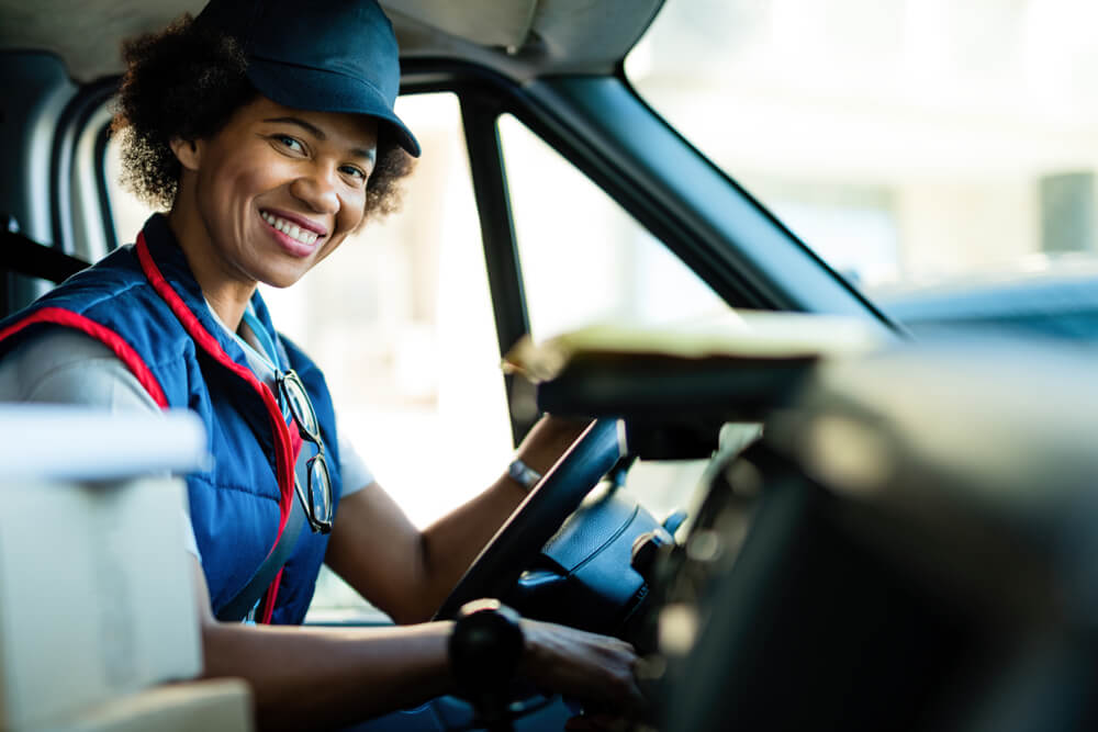 Happy black female courier driving delivery van and looking at camera