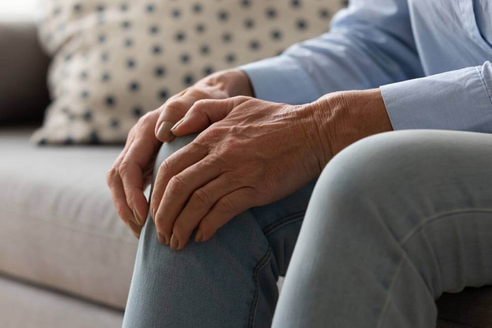 Elderly woman seated on couch touches knee