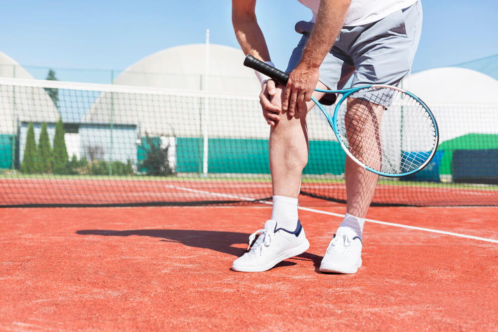 mature man holding tennis racket while suffering from knee pain