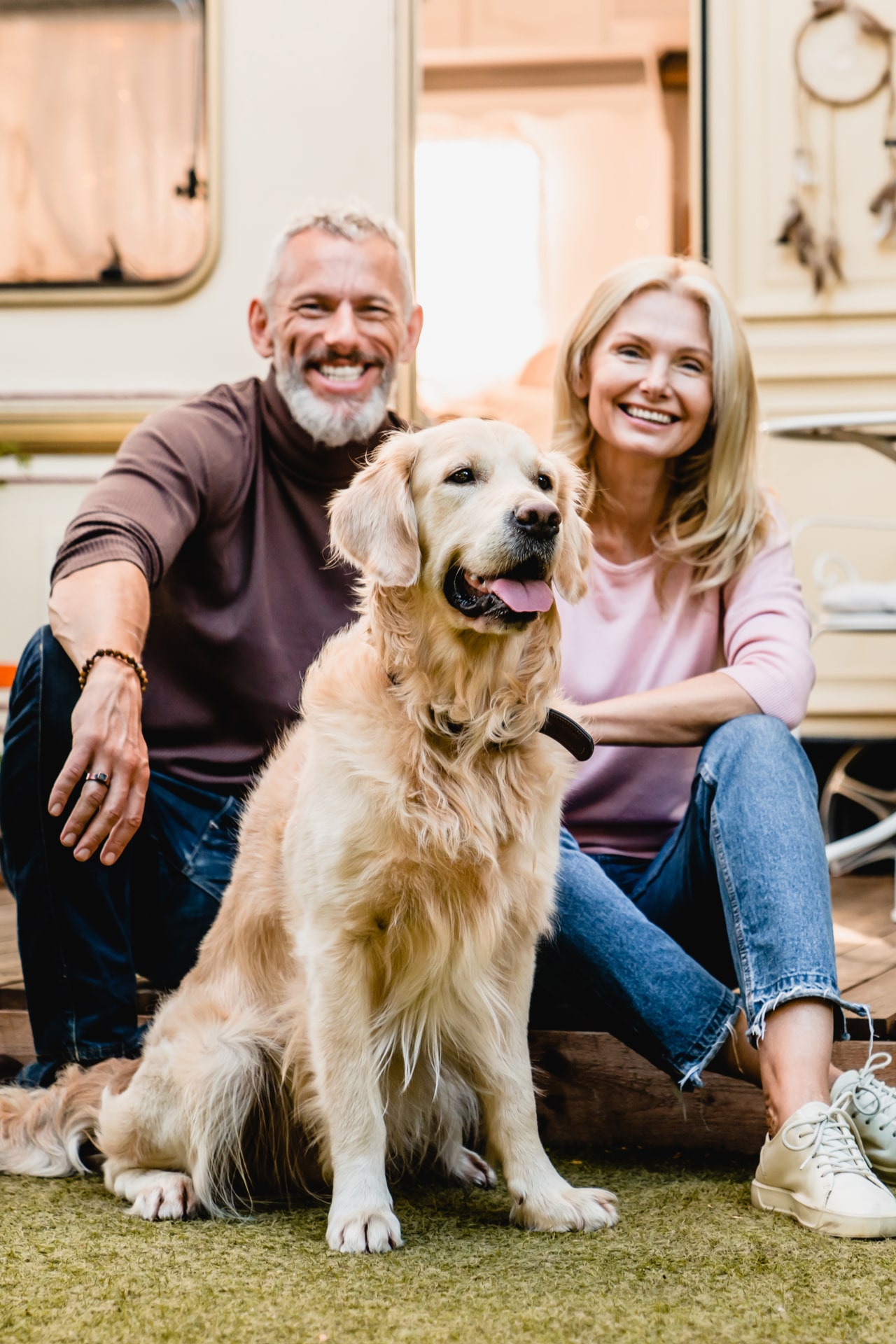 Happy aged european couple resting in the yard with their dog with motorhome in the background