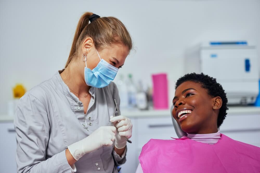 A mature dentist and his lovely young assistant standing in his consultation room while a young patient sits in the chair