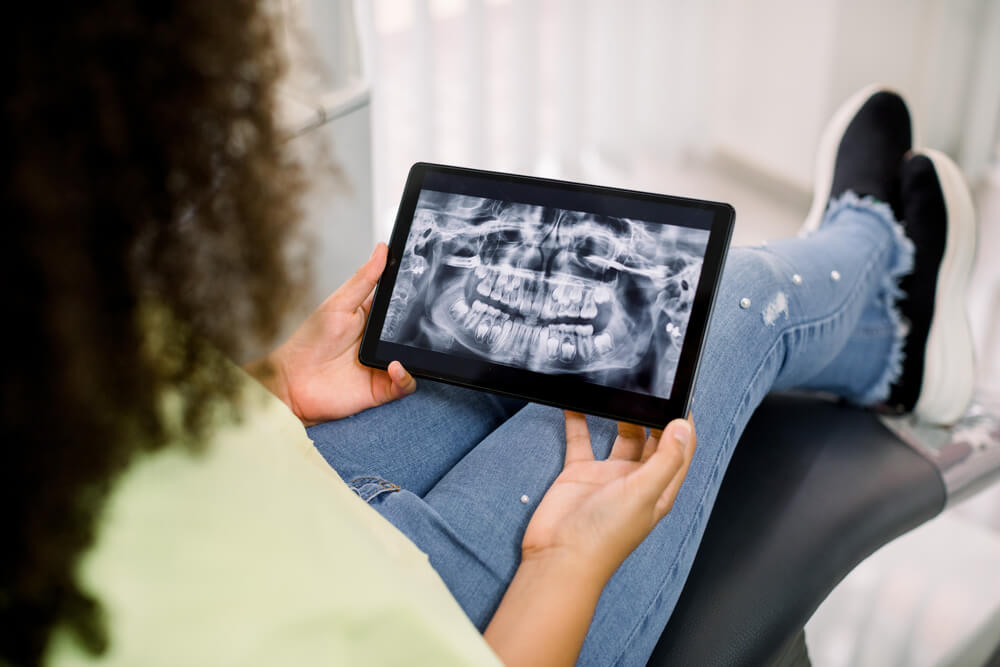 teen girl, sitting in dental chair at modern clinic, holding digital tablet