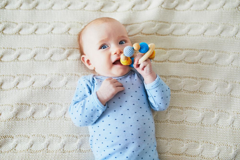 Newborn baby girl playing with colorful teething toy.