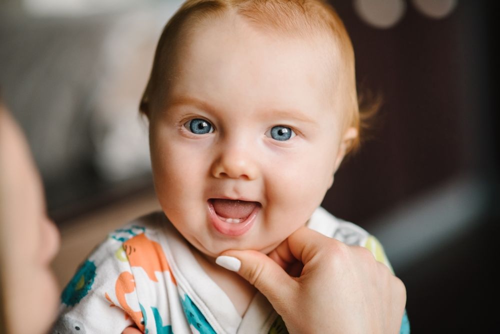 Close-up mother hands open baby mouth to examine first teeth.