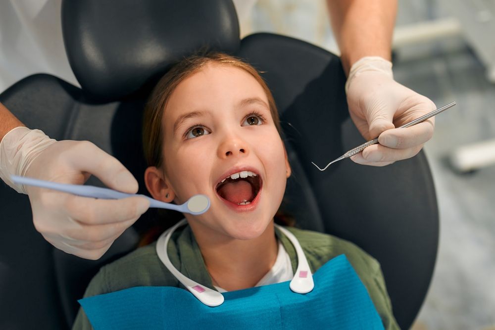 little girl sitting on a dental chair opening her mouth wide on examination by a pediatric dentist