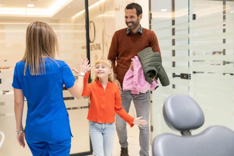A cheerful young girl high-fives a smiling dentist in a modern dental office, celebrating a successful dental visit