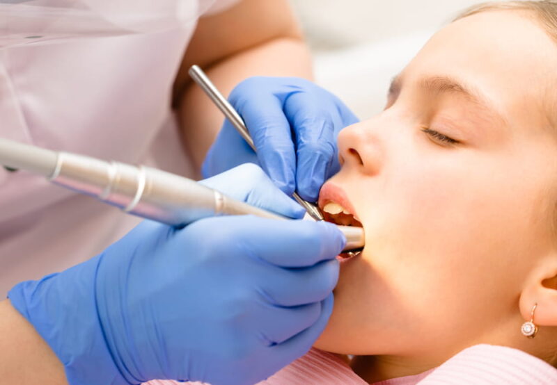 Dentist performing dental filling procedure to preteen girl in pediatric dental clinic