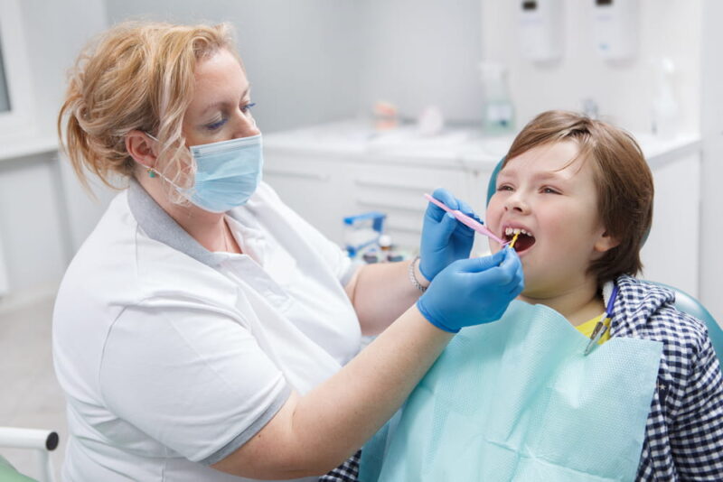 Professional dentist giving fluoride dental treatment to a young boy
