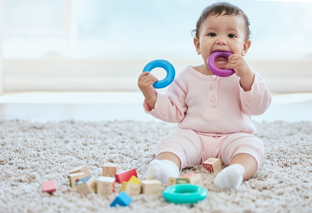 Baby, portrait and playing with toy on floor in home for sensory development, teething progress and biting