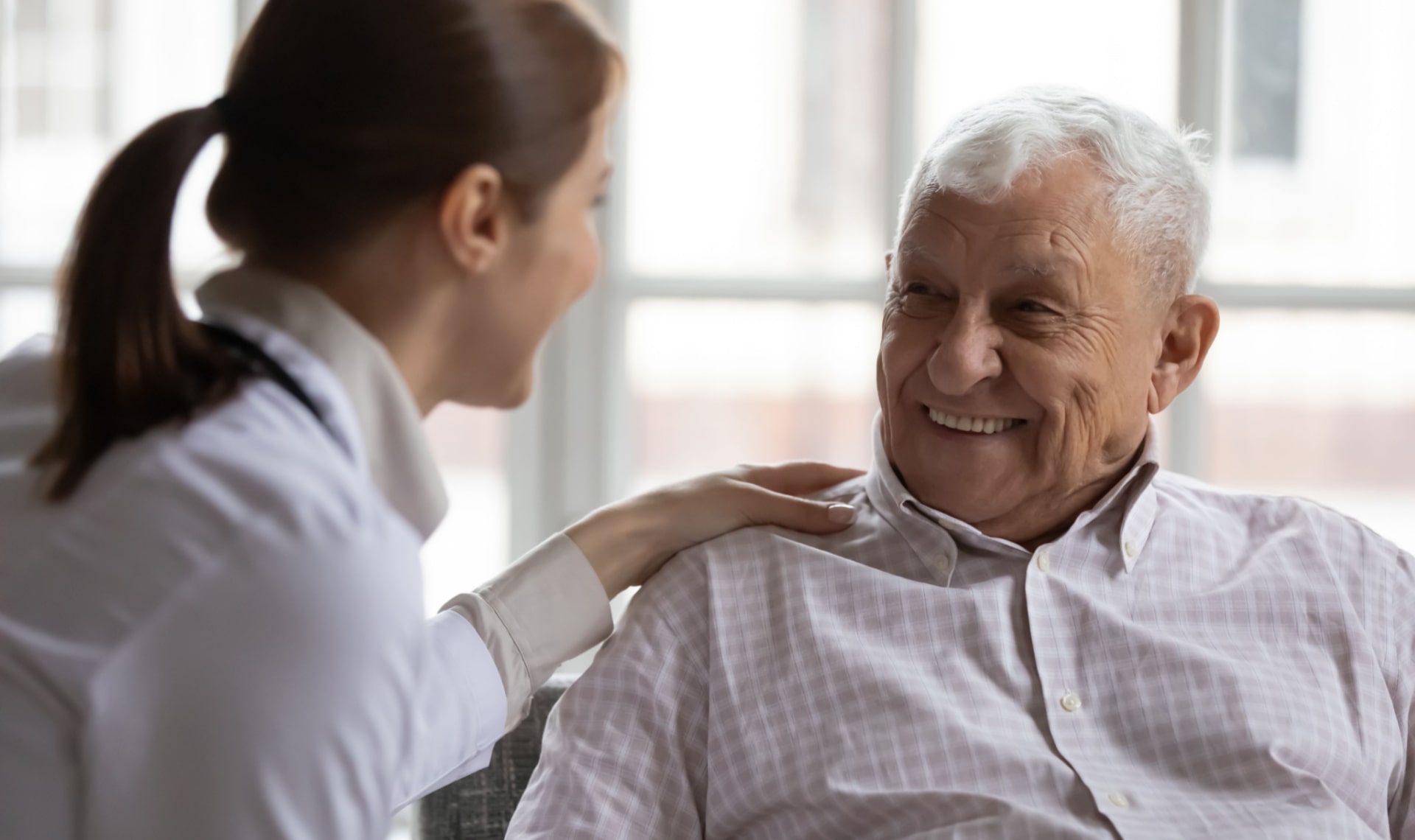 Caring geriatric nurse in white coat cares for grey-haired elderly man
