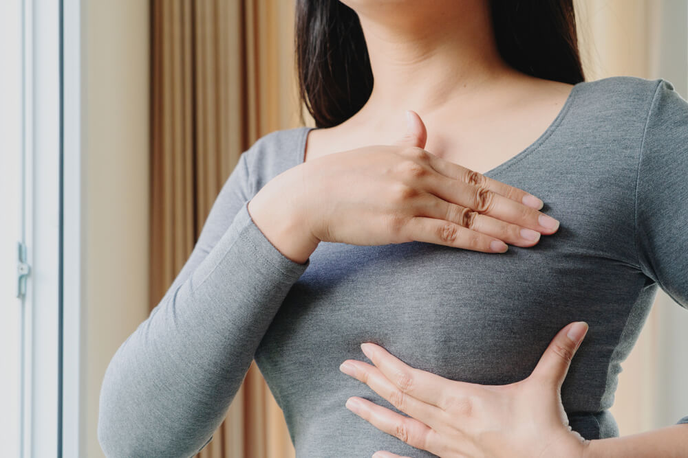 Woman hand checking lumps on her breast for signs of breast cancer.
