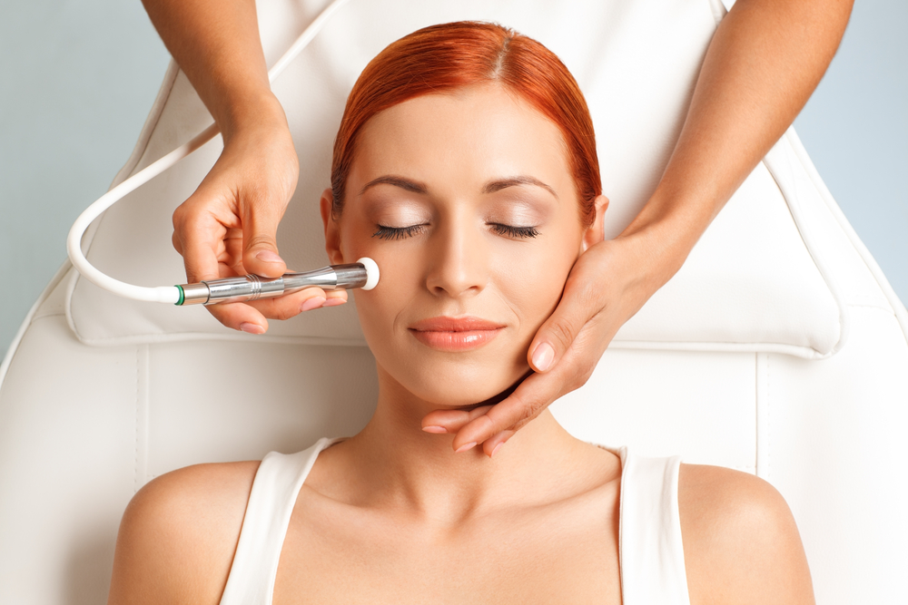 closeup portrait of lovely redheaded woman with closed eyes getting microdermabrasion procedure in a beauty salon