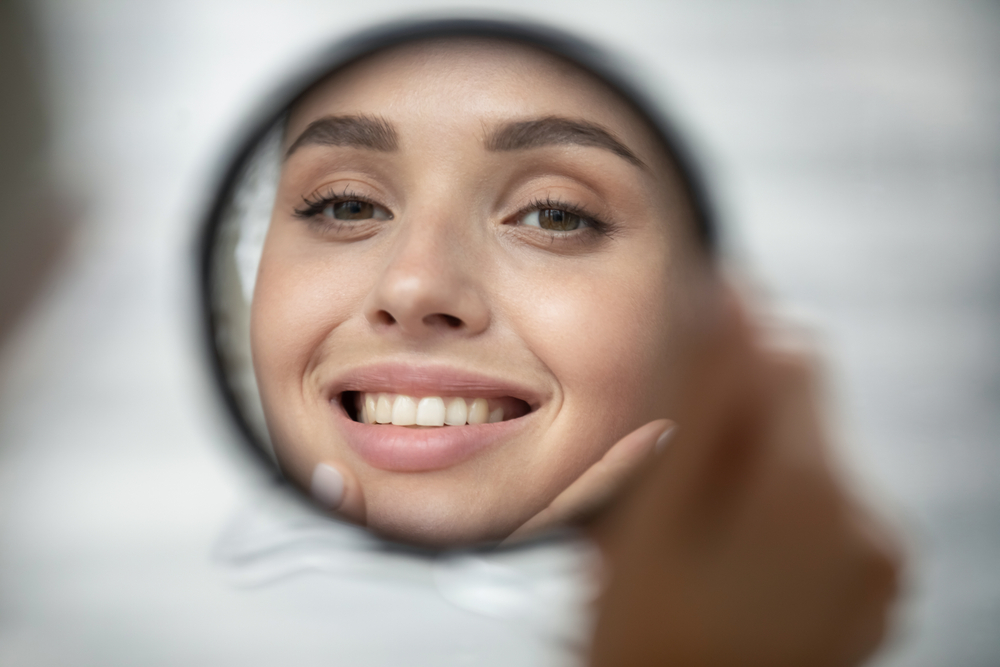 women smiling in the mirror after a Kybella Treatment