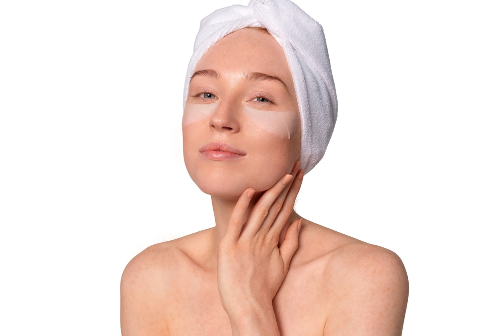 Skin care routine featuring a young woman applying facial mask while wearing a towel on her head
