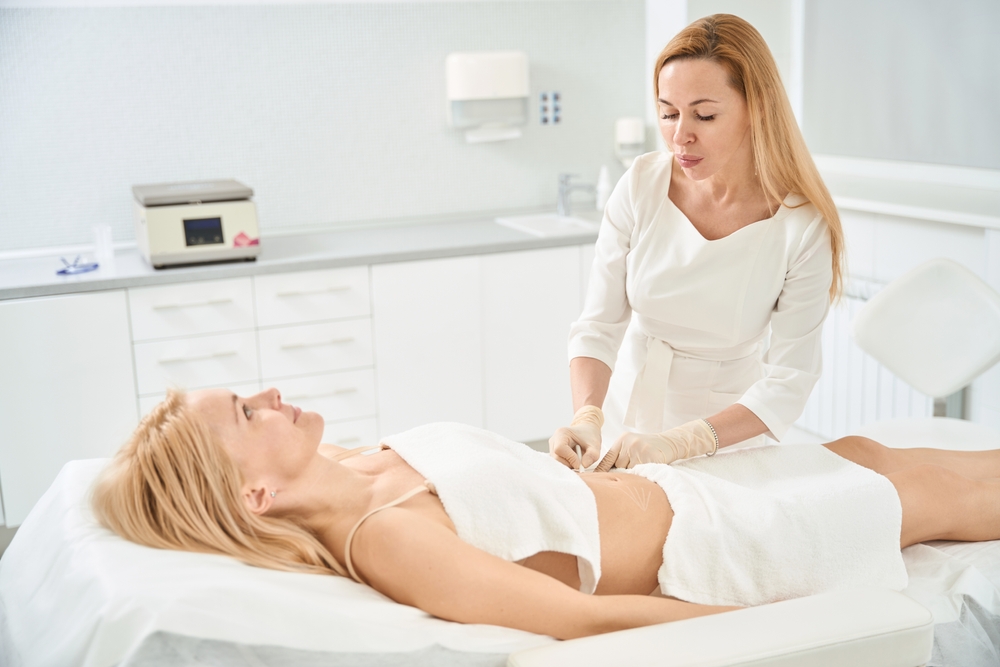 Qualified therapist making marks on body of client, tummy tuck with mesothreads