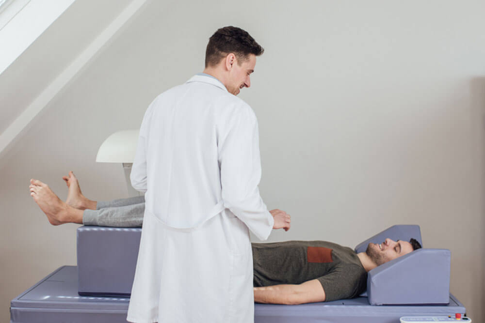 Young Caucasian medical technician operating the bone densitometer while his patient is lying on the bed.