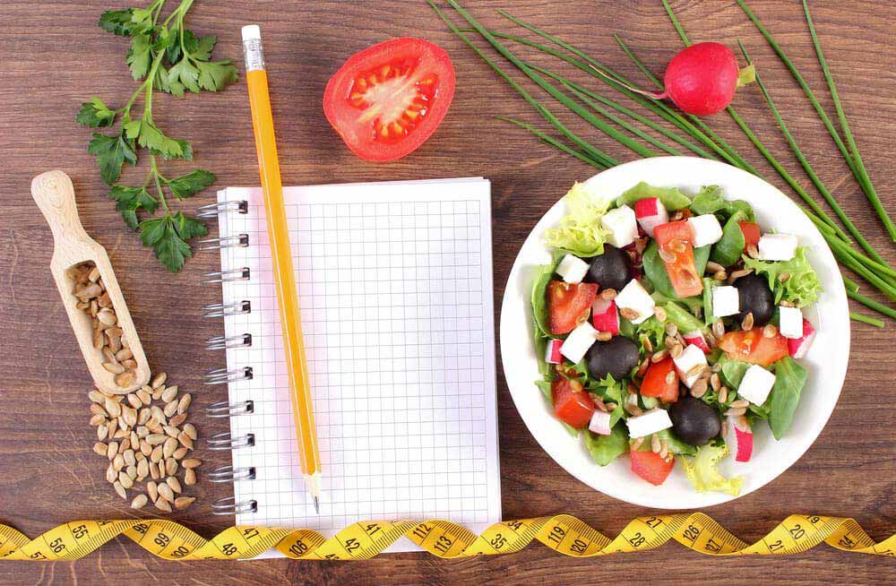 Fresh greek salad with vegetables, tape measure and notepad for writing notes