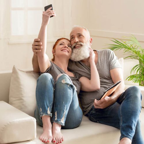 Happy mature couple taking selfie while sitting on sofa at home