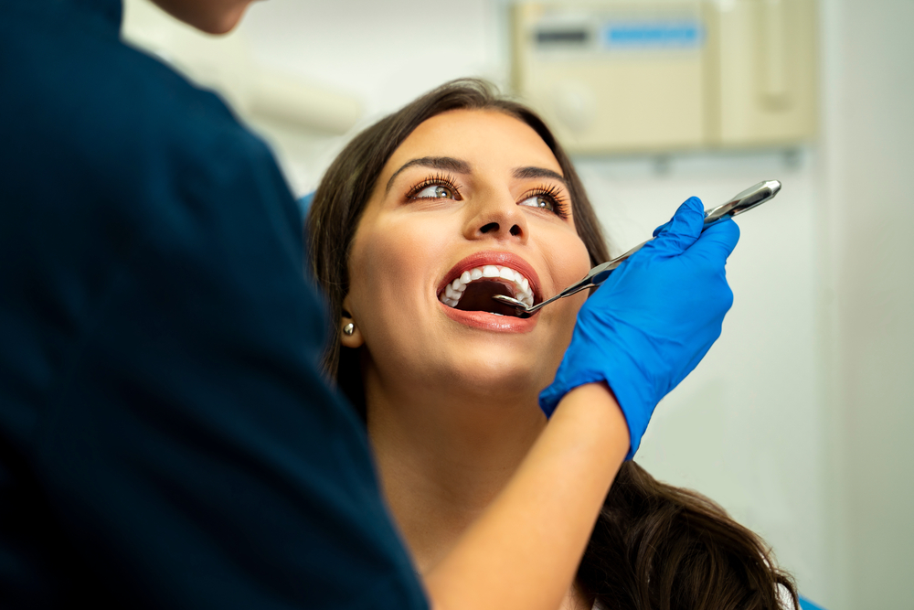 Happy, relaxed young woman in routine dental checkup. Smiling while dentist holding mirror tool, closeup shot