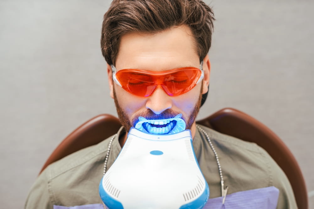 middle aged man sitting in dental chair wearing red eyeglasses with open mouth, teeth whitening