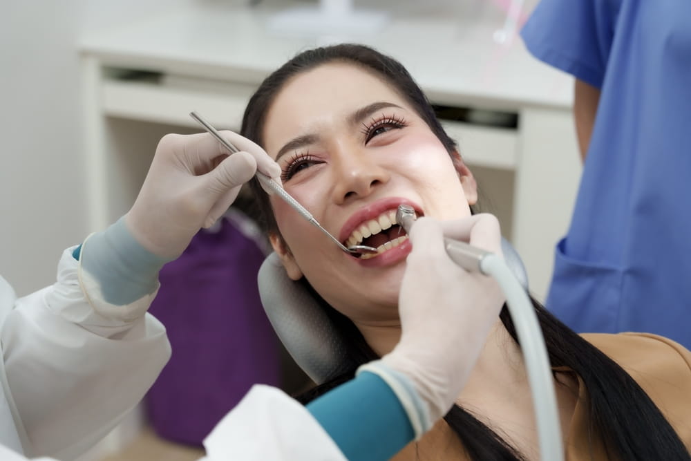 emaledentist using dental mirror and scaler examining mouth of asian adult female sitting in chair