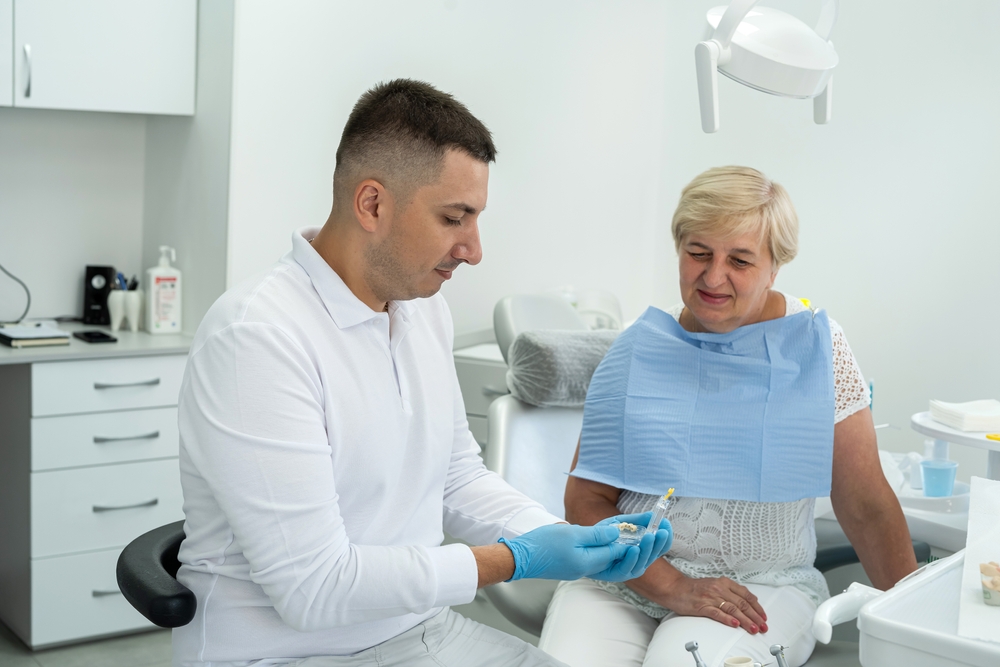 dentist holds an implant and consults an elderly woman with the installation of a tooth crown, dental clinic