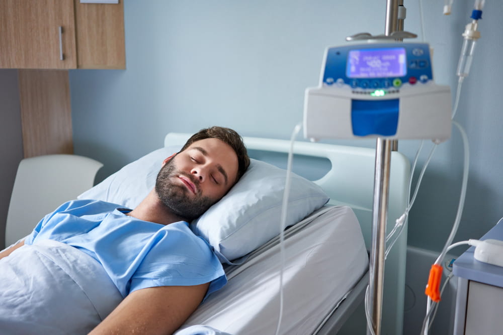 Young man attached to an intravenous drip sleeping on a bed in a hospital room