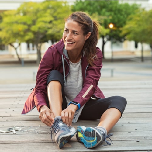 Mature fitness woman tie shoelaces on road.