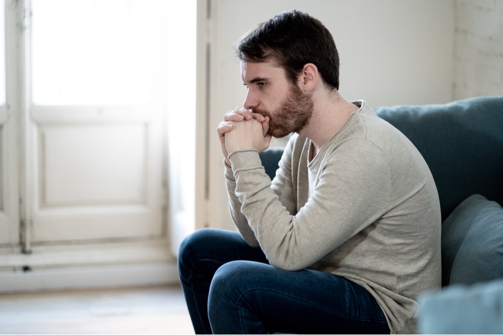 Unhappy depressed caucasian male sitting and lying in living room couch feeling desperate