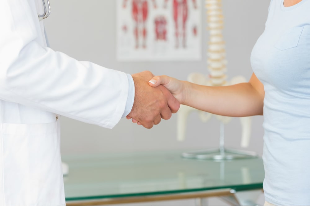 Close up of doctor shaking hands with patient in bright office