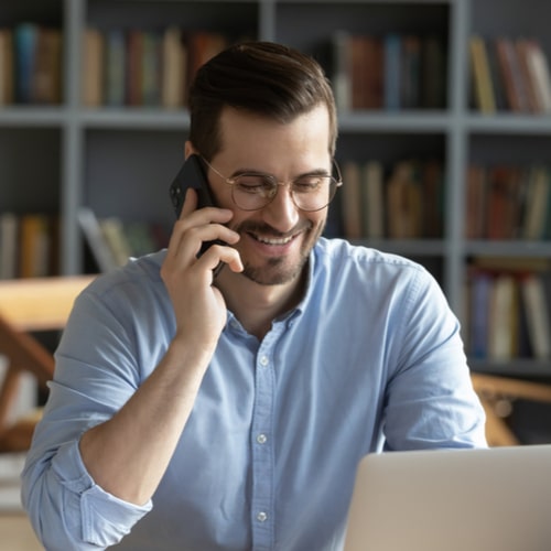 Smiling businessman wearing glasses talking on phone, sitting at desk with laptop