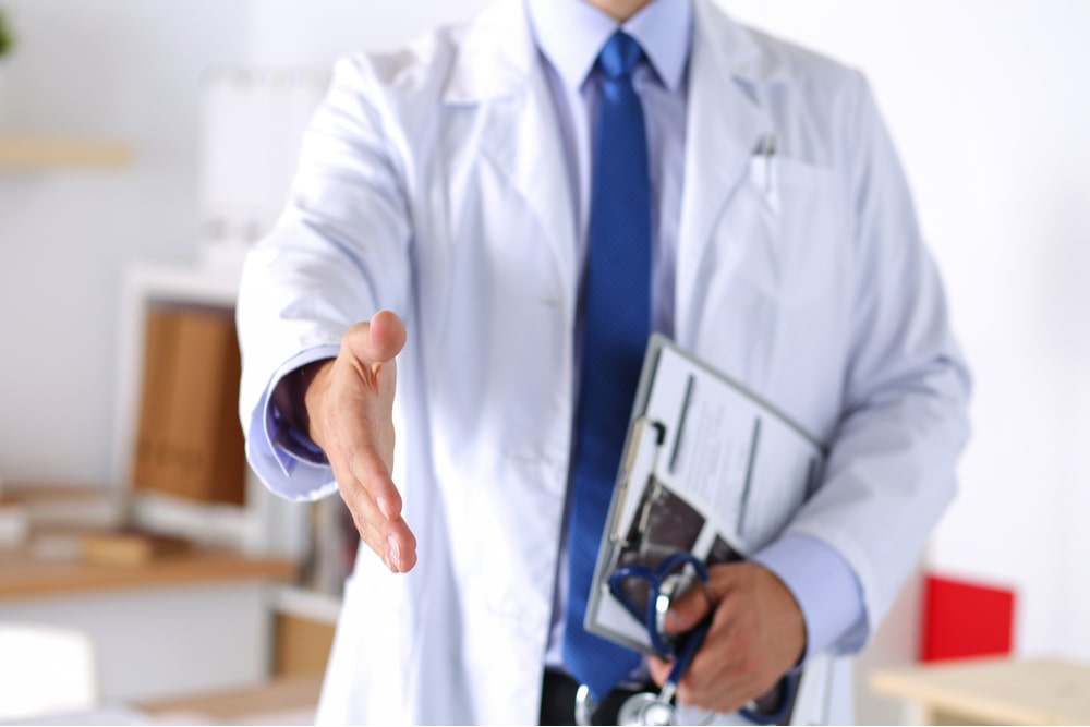 Male medicine doctor offering hand to shake in office closeup