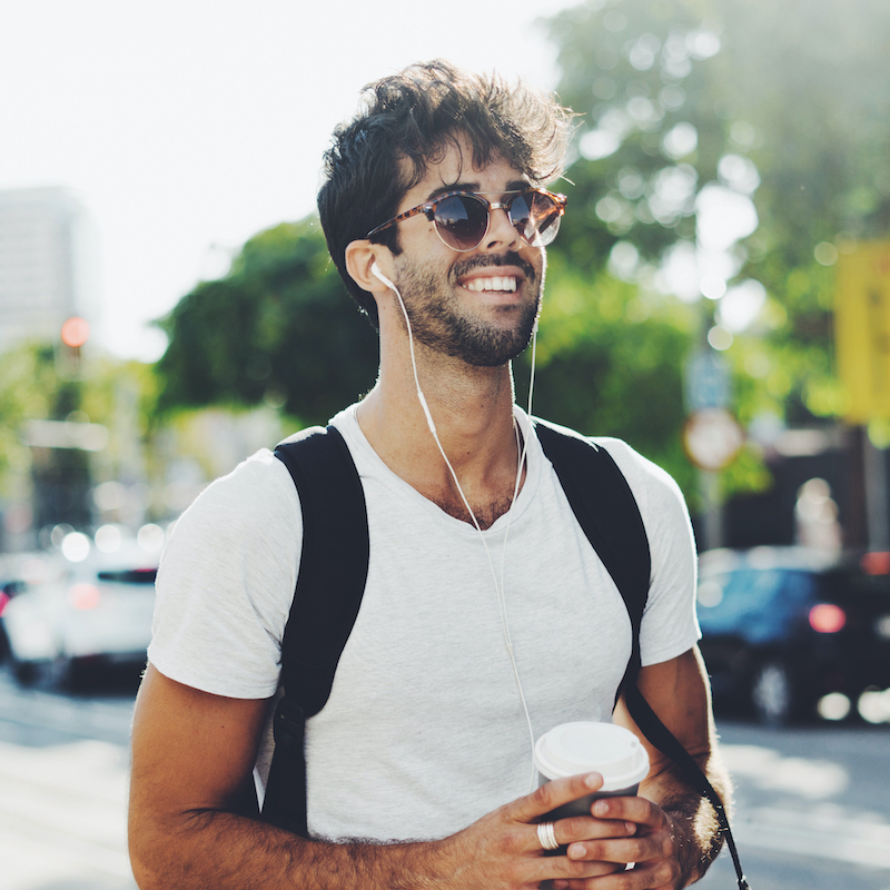 Man with sunglasses, a coffee cup, and earbuds, smiling