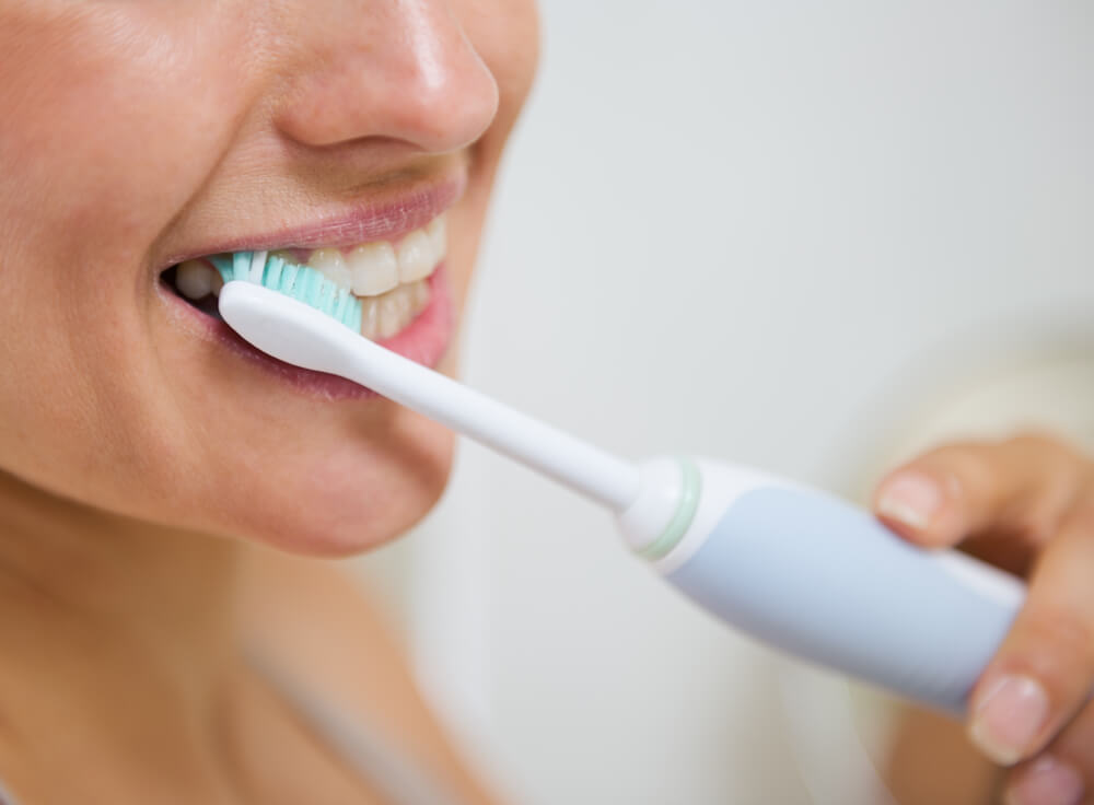 woman brushing her teeth with an electric toothbrush