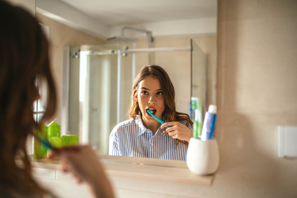 woman brushing her teeth in the bathroom mirror